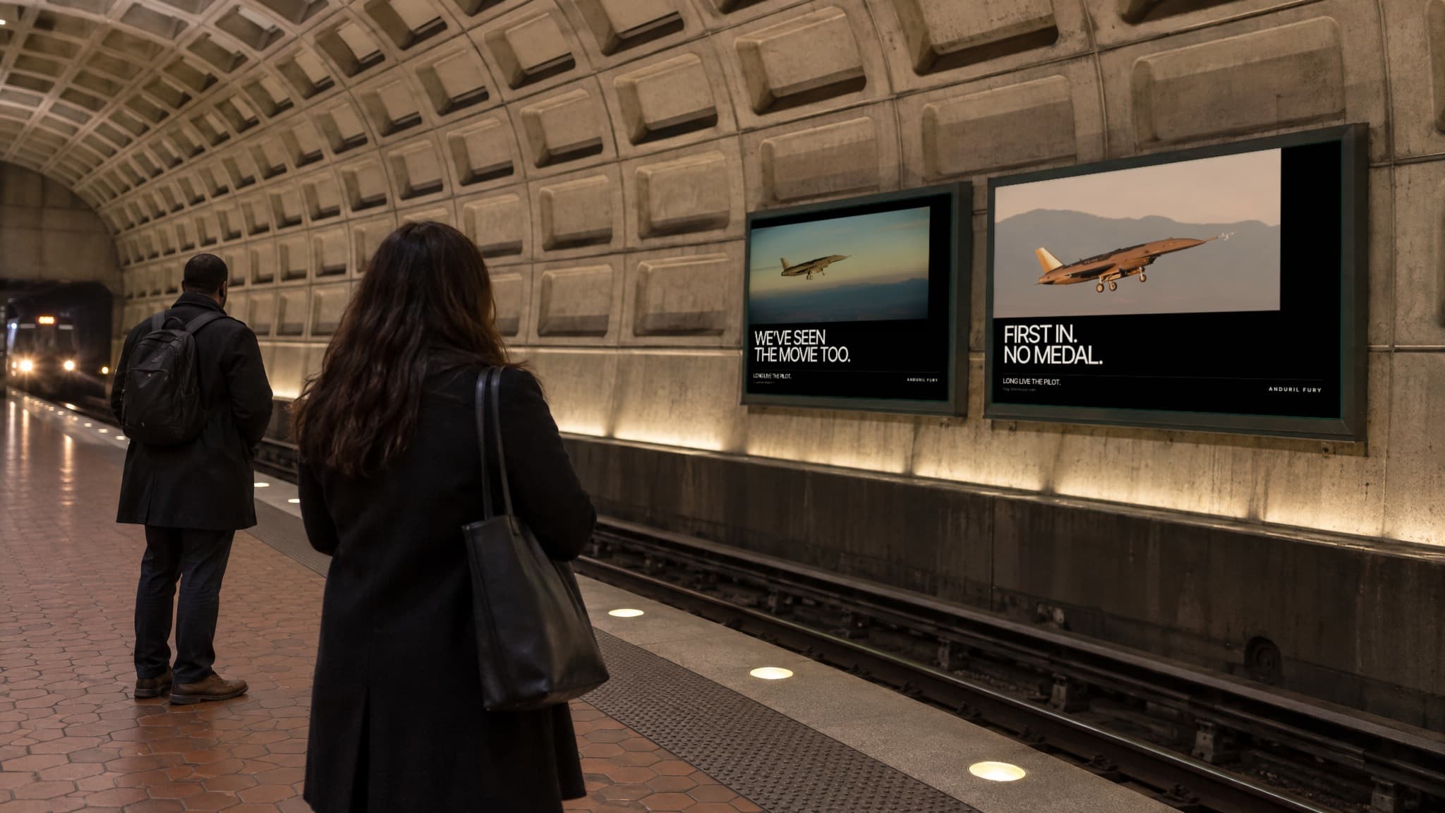 The two Metro posters on the vaulted wall of a station platform, WE'VE SEEN THE MOVIE TOO and FIRST IN. NO MEDAL, as two riders wait for a train