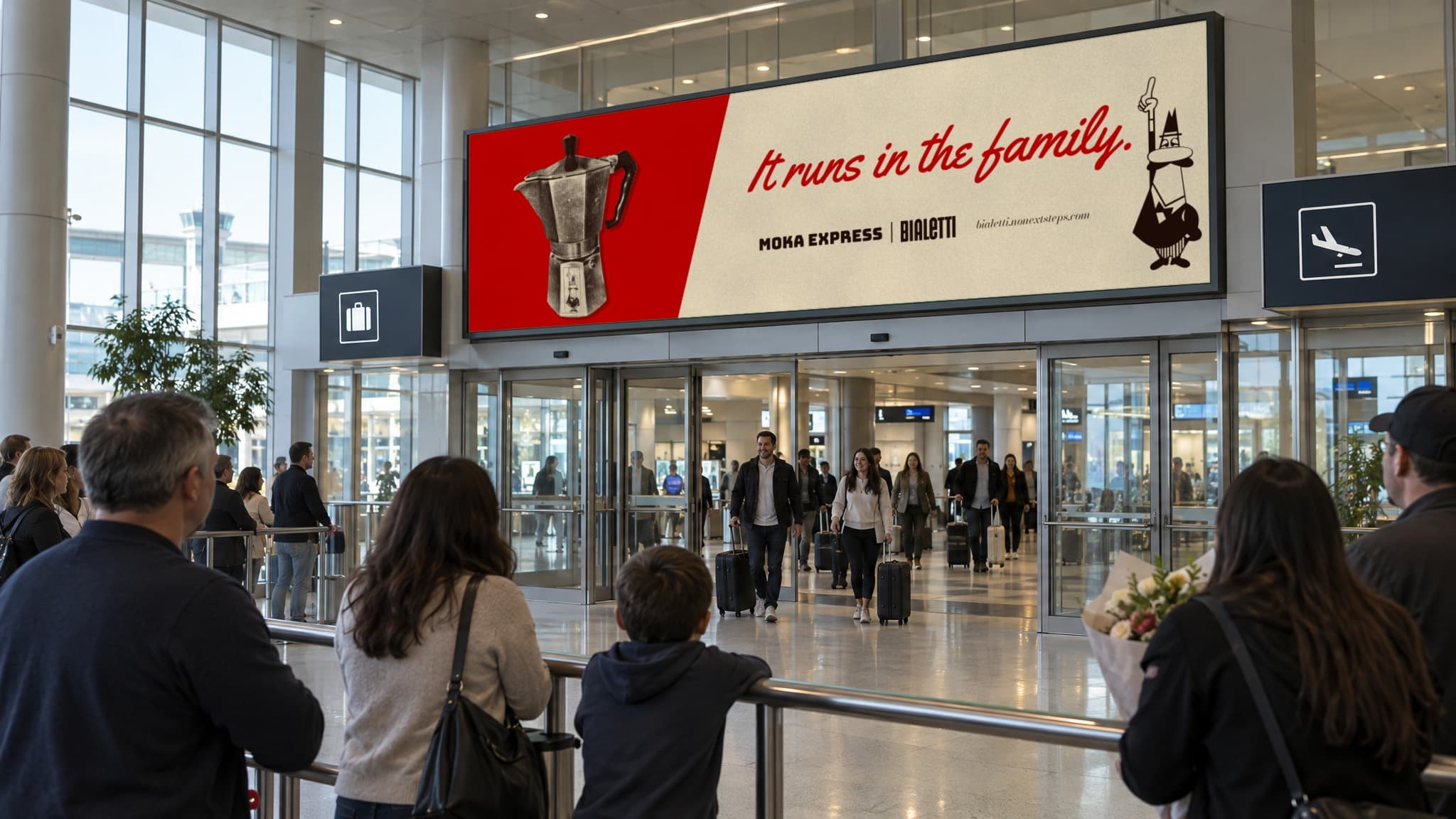 The screen over the doors of an airport arrivals hall reading It runs in the family. while families wait at the rail and travelers walk out with suitcases