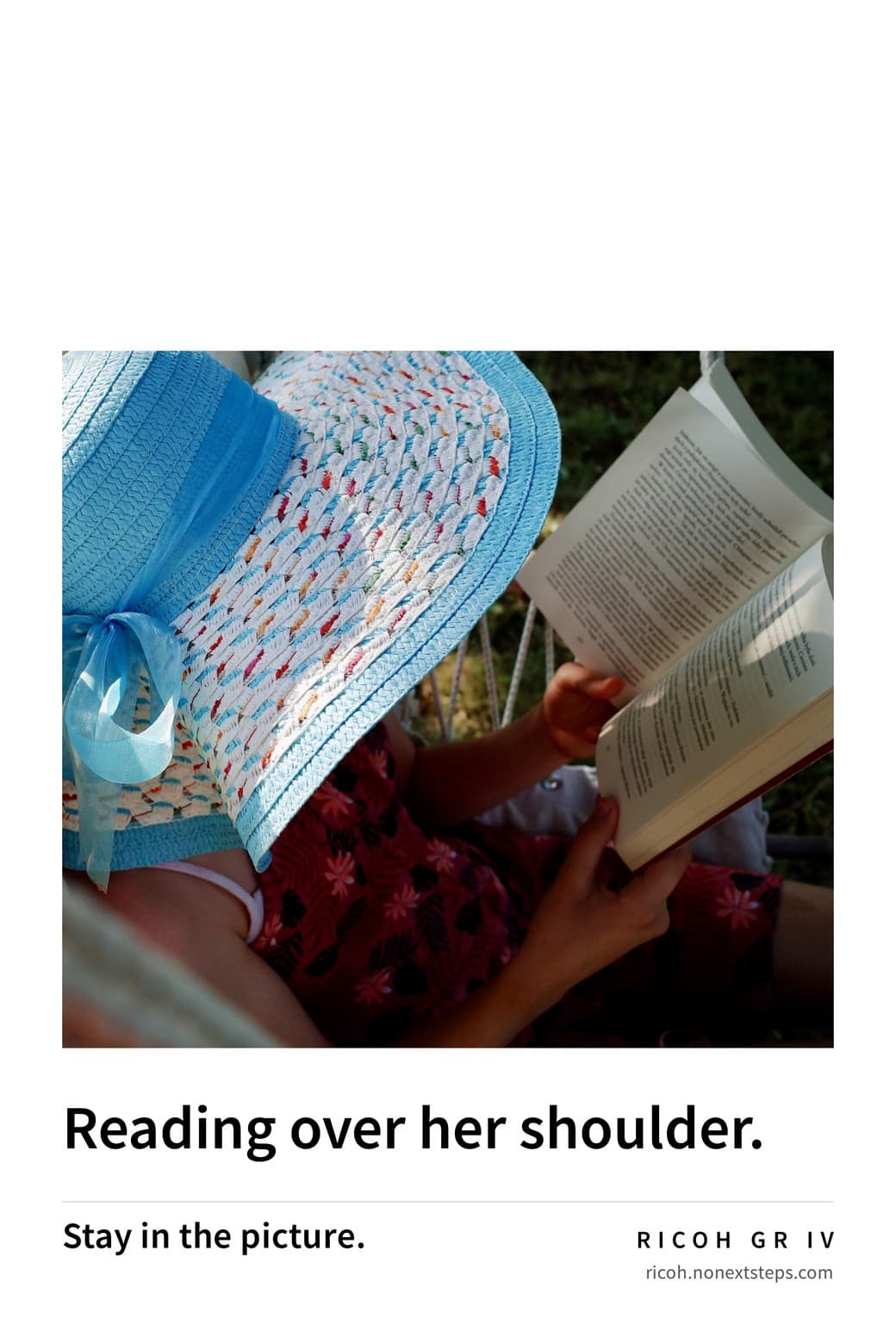 Poster: a child reading a book under a wide blue sun hat. Reading over her shoulder. Stay in the picture. RICOH GR IV